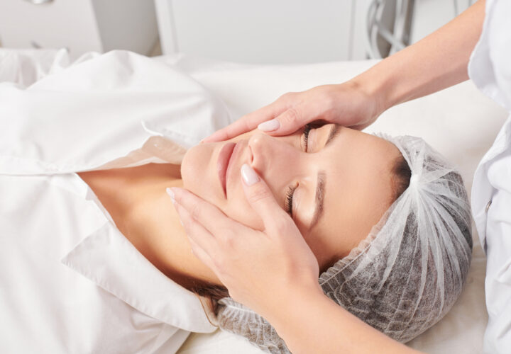 Cosmetologist massages woman face skin after rubbing moisturizing cream for rejuvenation, anti aging cosmetic procedure in beauty spa salon. Beautician hands massages female face for relax